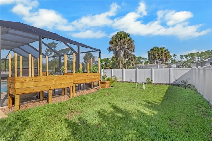 Screened enclosure with built-in raised garden beds, expansive lawn, white privacy fence, and mature palm trees