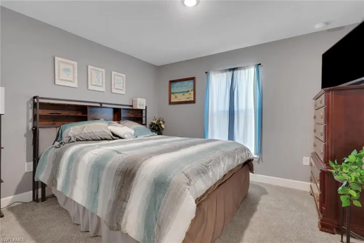 Carpeted bedroom featuring a window with sheer curtains, recessed lighting, and a wood-finish headboard with integrated shelving