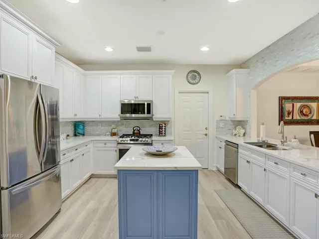 Kitchen featuring stainless steel appliances, white cabinets, light stone countertops, a center island, and light wood-type flooring