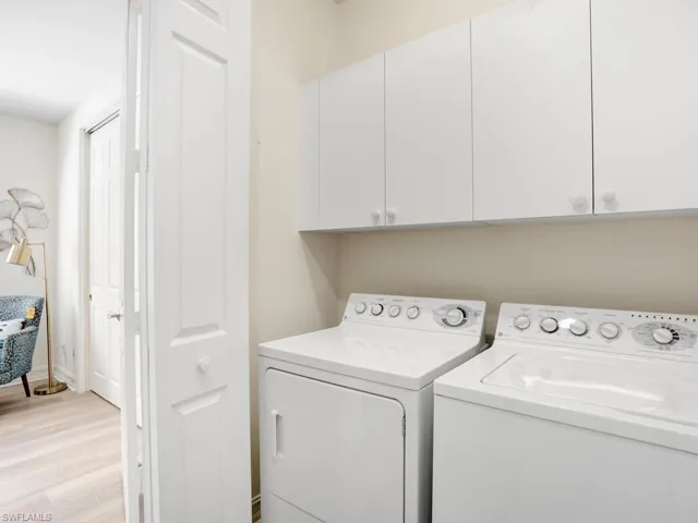 Washroom featuring light wood-type flooring, washing machine and dryer, and cabinet space
