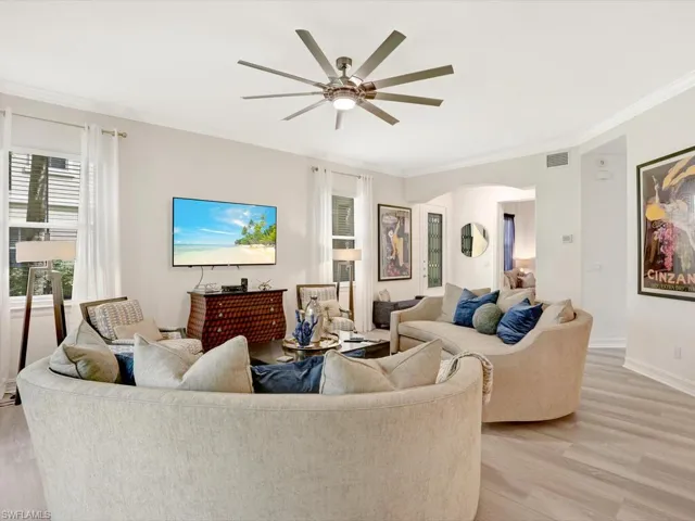 Living room featuring light wood-style floors, ornamental molding, a ceiling fan, and arched walkways