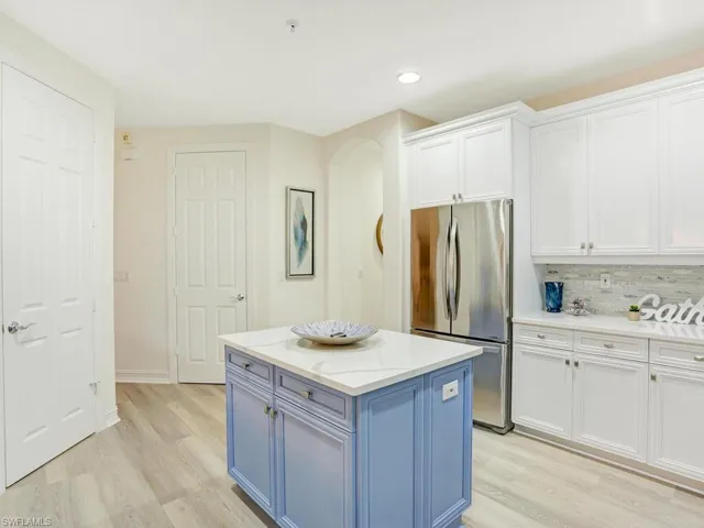 Kitchen with white cabinetry, blue cabinetry, freestanding refrigerator, light stone counters, and light wood-style floors