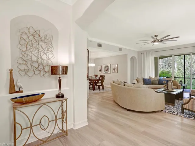 Living room featuring light wood finished floors, ornamental molding, a ceiling fan, and arched walkways