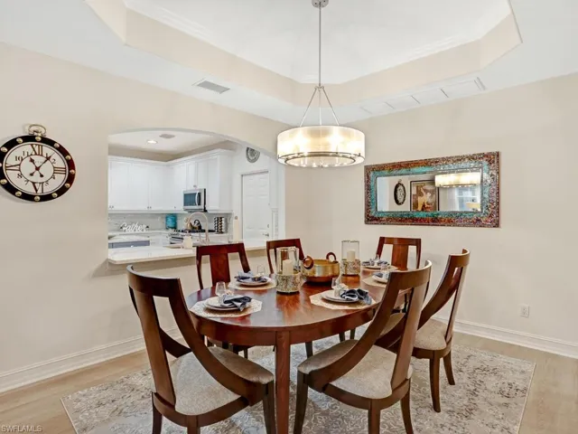 Dining space featuring light wood-type flooring, arched walkways, a tray ceiling, and crown molding