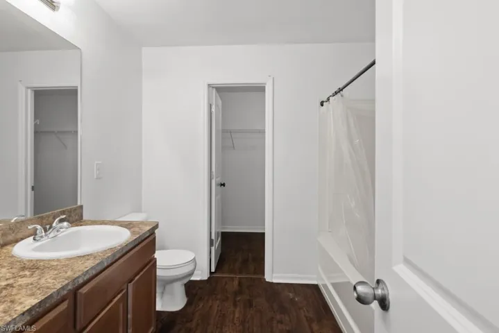 Bathroom with vanity, a walk in closet, dark wood-type flooring, and shower / bath combination with curtain