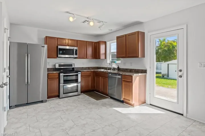 Kitchen featuring stainless steel appliances, wood finish cabinetry, light marble finish floors, rail lighting, and dark stone counters