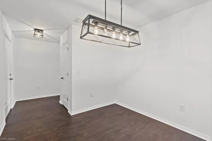 Unfurnished dining area featuring dark wood-style flooring and baseboards
