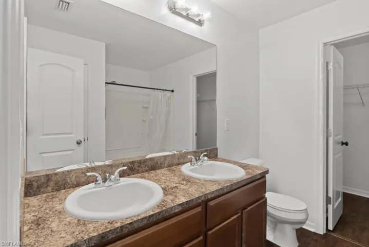 Bathroom featuring a spacious closet, double vanity, a shower with curtain, and dark wood finished floors