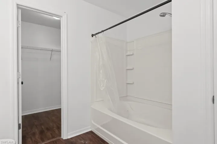 Bathroom with shower / bath combination with curtain, a walk in closet, and dark wood-style floors
