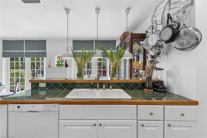 Kitchen with dishwashing machine, tile counters, white cabinetry, decorative backsplash, and pendant lighting
