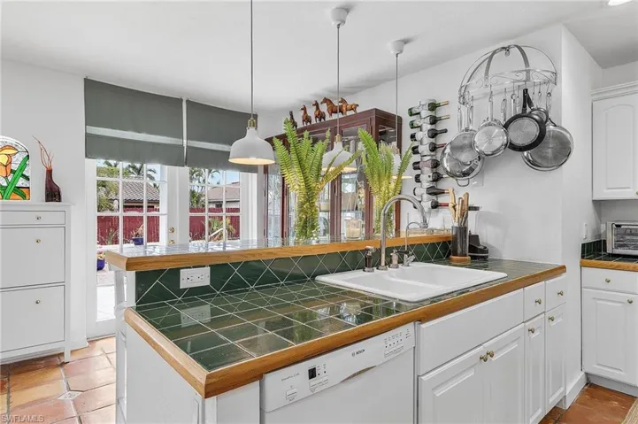 Kitchen featuring white cabinets, white dishwasher, a peninsula, decorative light fixtures, and light tile patterned floors