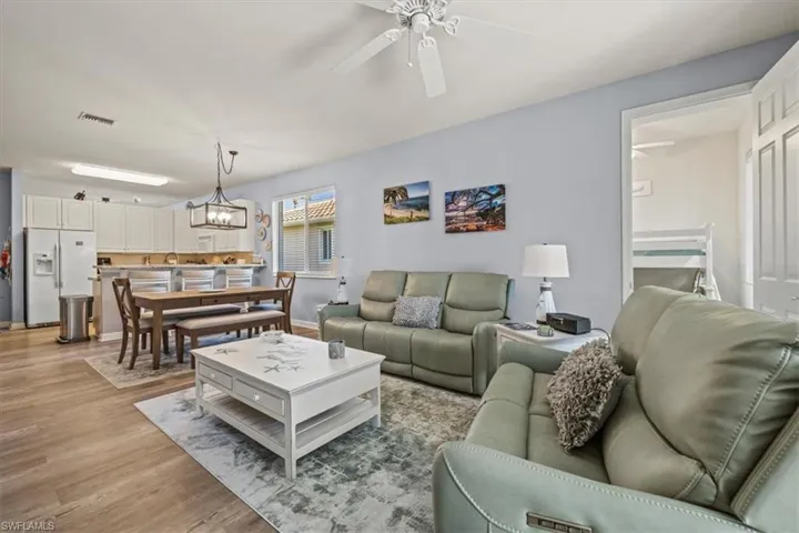 Living room with light wood-type flooring, visible vents, and ceiling fan with notable chandelier