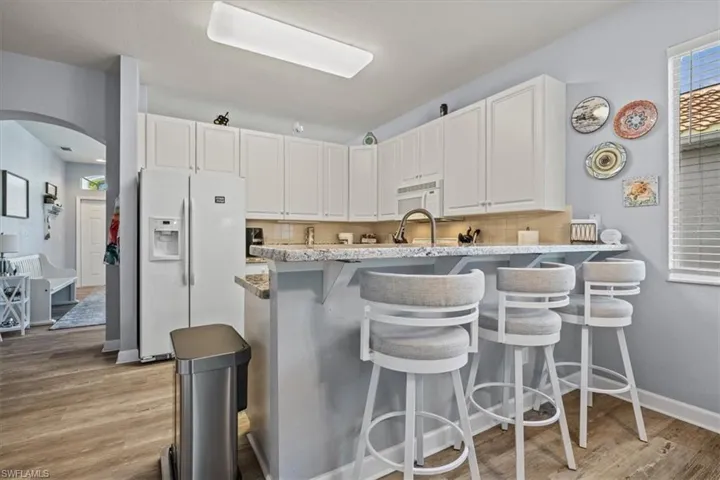 Kitchen with light wood-type flooring, white appliances, backsplash, and white cabinetry