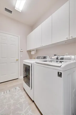 Laundry area featuring visible vents, baseboards, light wood-style flooring, cabinet space, and independent washer and dryer