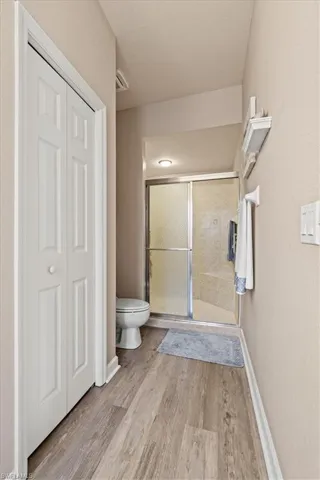 Bathroom featuring toilet, a stall shower, wood finished floors, a closet, and baseboards