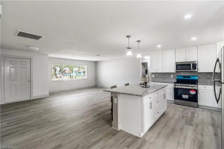 Kitchen with pendant lighting, white cabinets, stainless steel appliances, a center island, and light hardwood / wood-style floors