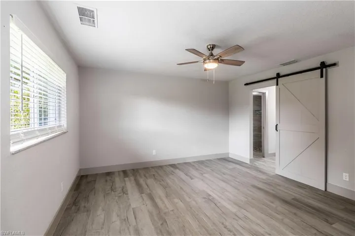 Unfurnished bedroom with ceiling fan, a textured ceiling, light hardwood / wood-style flooring, and a barn door