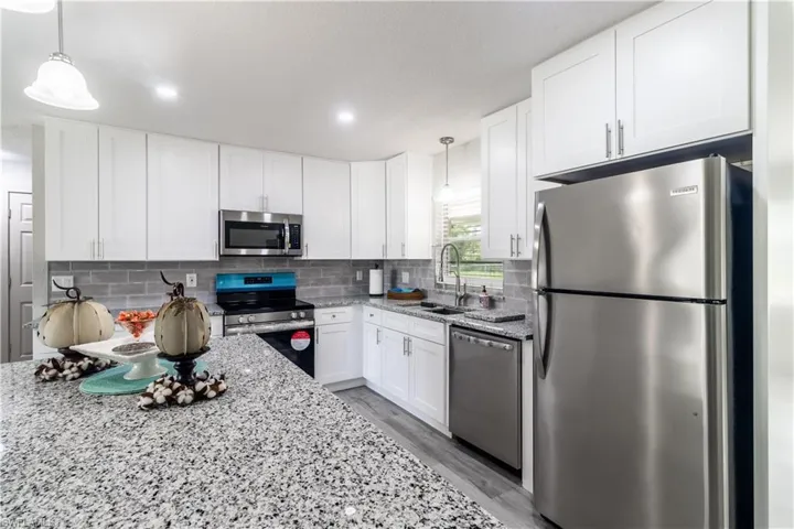 Kitchen featuring light stone counters, stainless steel appliances, white cabinets, light hardwood / wood-style flooring, and decorative light fixtures