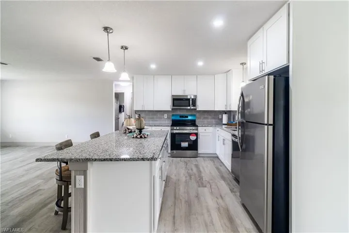 Kitchen featuring a kitchen island, stainless steel appliances, white cabinets, light hardwood / wood-style floors, and a kitchen bar