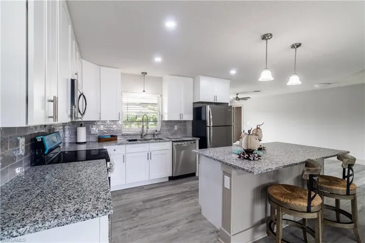 Kitchen with decorative light fixtures, a kitchen island, appliances with stainless steel finishes, and white cabinetry