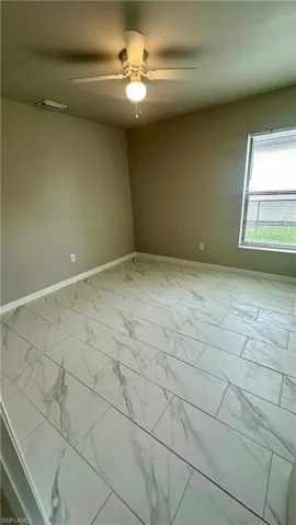 Unfurnished room featuring marble look tiles and a ceiling fan