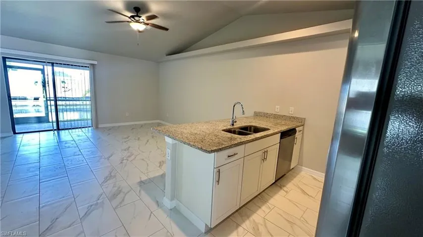 Kitchen featuring light marble finish floors, ceiling fan, light stone countertops, vaulted ceiling, and white cabinetry