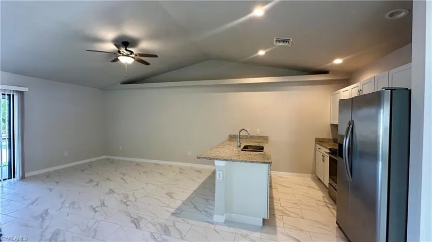 Kitchen with appliances with stainless steel finishes, light marble finish flooring, a peninsula, a ceiling fan, and light stone countertops