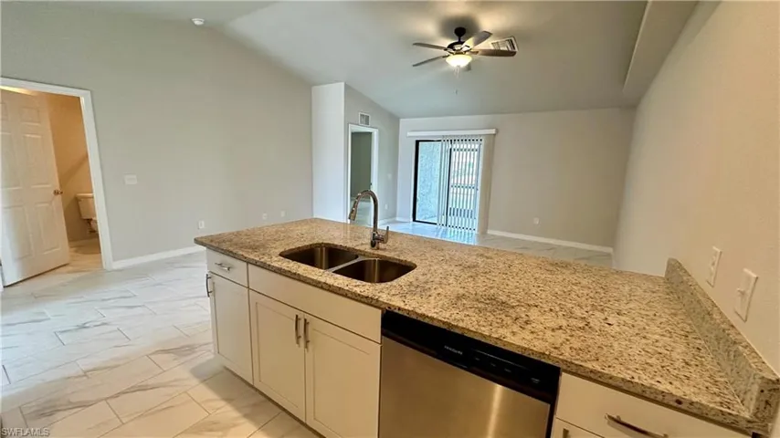 Kitchen with light marble finish flooring, dishwasher, lofted ceiling, light stone countertops, and ceiling fan