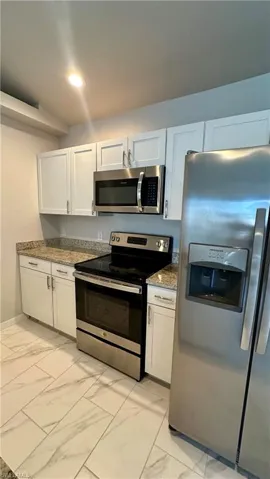 Kitchen featuring light marble finish floors, stainless steel appliances, stone counters, white cabinetry, and recessed lighting