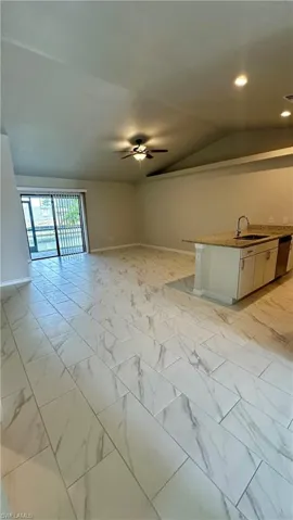 Unfurnished living room featuring light marble finish flooring, ceiling fan, and lofted ceiling