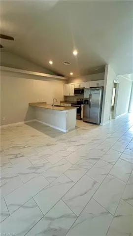 Kitchen with light marble finish floors, stainless steel appliances, a peninsula, vaulted ceiling, and recessed lighting