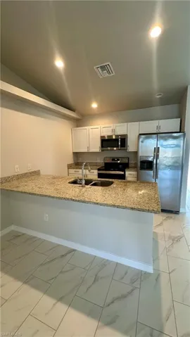 Kitchen with light marble finish floors, stainless steel appliances, light stone counters, a peninsula, and white cabinetry