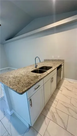 Kitchen featuring light marble finish flooring, stone countertops, vaulted ceiling, dishwasher, and a peninsula