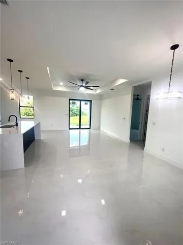 Unfurnished living room with a tray ceiling, ceiling fan, and sink