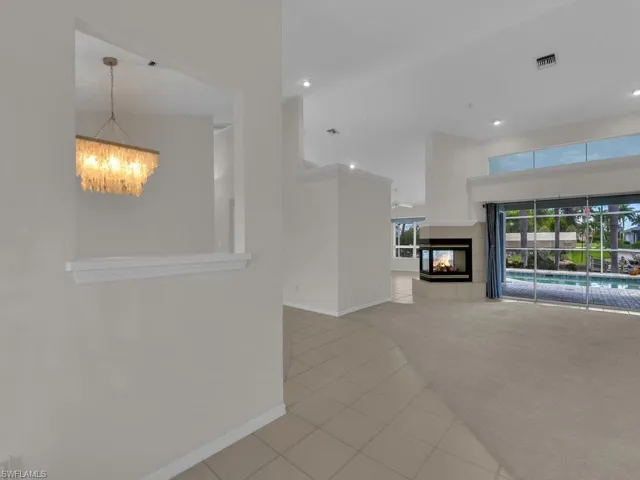Spacious interior featuring a contemporary fireplace with an elevated hearth, large sliding glass doors, a decorative overhead chandelier, high ceilings, and transom windows