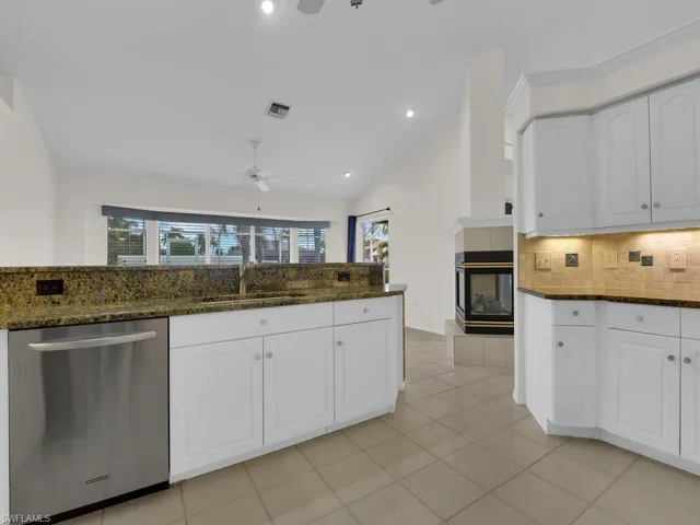 Kitchen featuring white cabinetry, stone countertops, a stainless steel dishwasher, and tile flooring