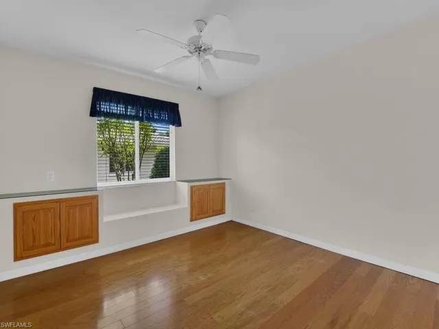 Room featuring rich wood-finish flooring, a ceiling fan, and a window with blinds