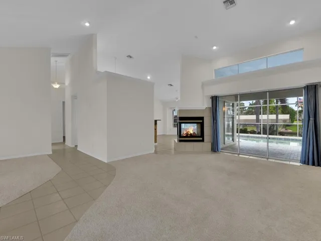 Expansive interior featuring a contemporary fireplace, large sliding glass doors, upper transom windows, recessed lighting, and a combination of carpet and tile flooring
