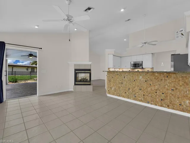 Spacious interior featuring tile flooring, a fireplace with a white mantel, and a kitchen with white cabinetry and stainless steel appliances