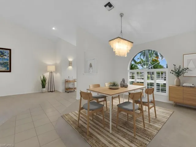 Spacious dining area featuring an arched window with white plantation shutters, a contemporary chandelier, vaulted ceilings, and tile flooring