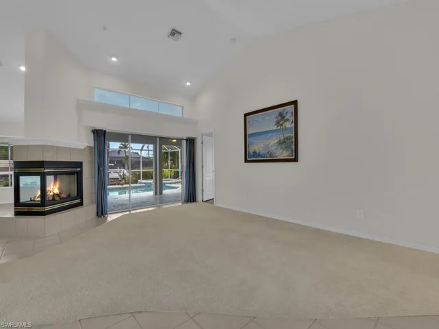 Vaulted ceiling interior featuring a corner fireplace with a tiled surround, sliding glass doors, transom windows, and recessed lighting