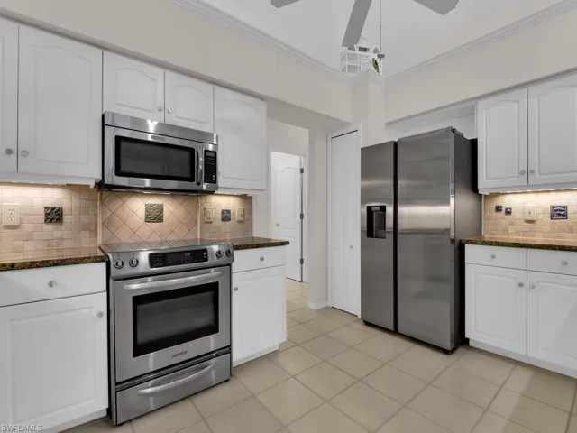 Kitchen featuring white cabinetry, granite countertops, tile backsplash, stainless steel appliances, and tile flooring