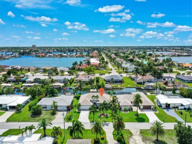 Waterfront property featuring a private boat dock, mature palm trees, manicured lawn, and a paved driveway