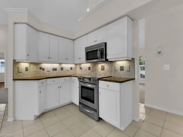 Kitchen featuring white cabinetry with brushed nickel hardware, stainless steel appliances, dark countertops, and a tiled backsplash
