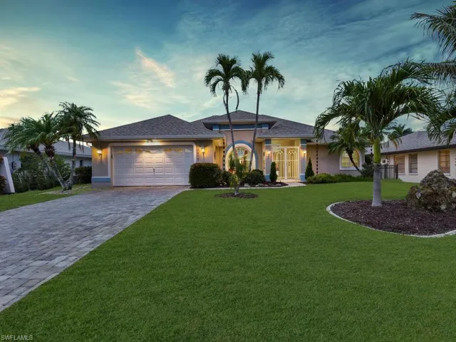 Single-story residence featuring a paver driveway, well-maintained lawn, and established palm trees