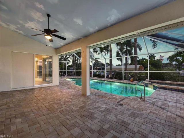 Spacious screened lanai featuring extensive paver flooring, an illuminated swimming pool with a handrail, an attached spa, and a ceiling fan