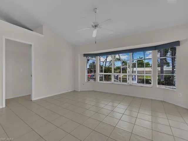 Spacious interior room featuring a wide bay window, vaulted ceiling, and neutral-toned tile flooring