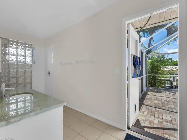 Bathroom featuring a vanity with a light-colored countertop and undermount sink, a glass block shower enclosure, tile flooring, and direct access to an outdoor screened lanai with paver flooring