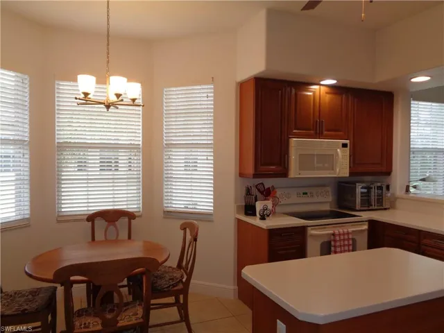 Kitchen featuring white appliances, light tile patterned flooring, light countertops, pendant lighting, and a center island