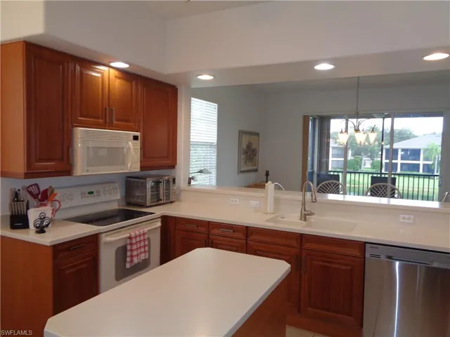 Kitchen featuring white appliances, recessed lighting, a peninsula, brown cabinetry, and hanging light fixtures